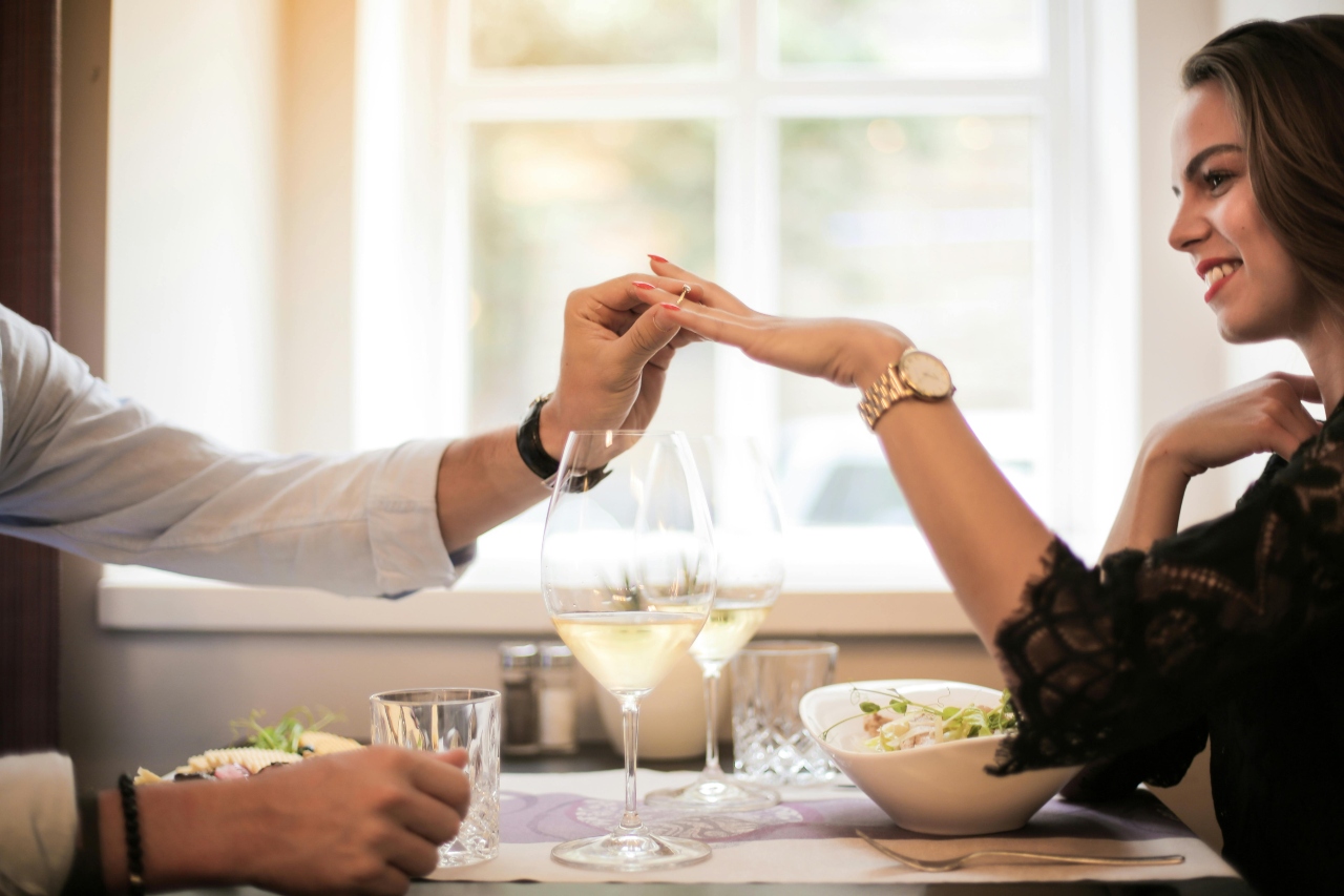 A man sliding a ring on a woman's finger in a cozy restaurant setting.