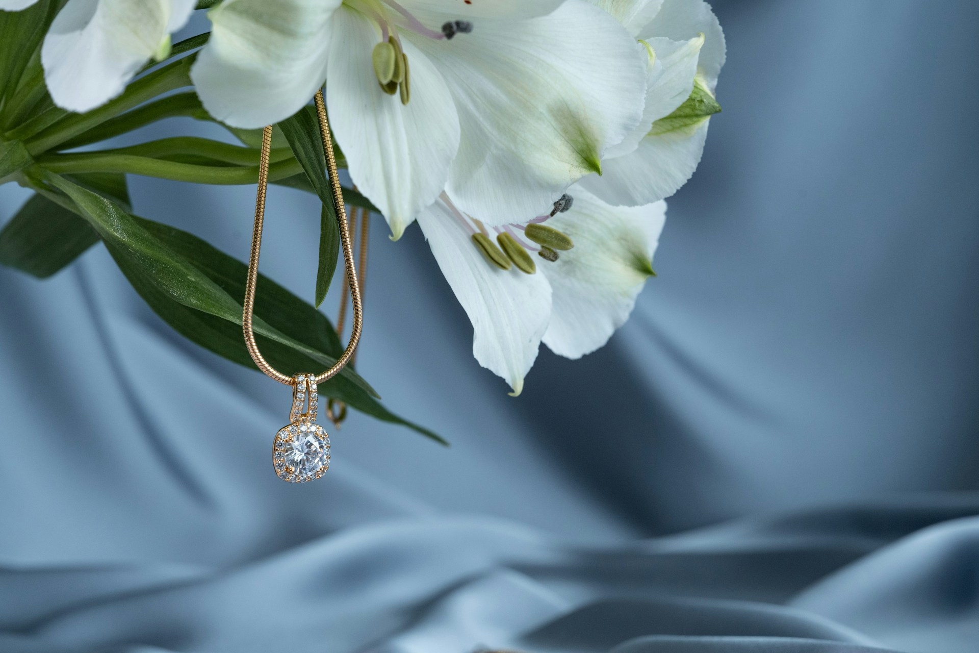 A yellow gold diamond pendant necklace hanging from a bouquet of white lilies.