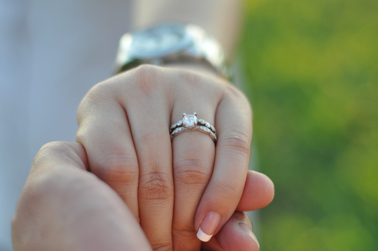A close up of a white gold bridal set with diamond center stone on a woman&rsquo;s hand with french manicure