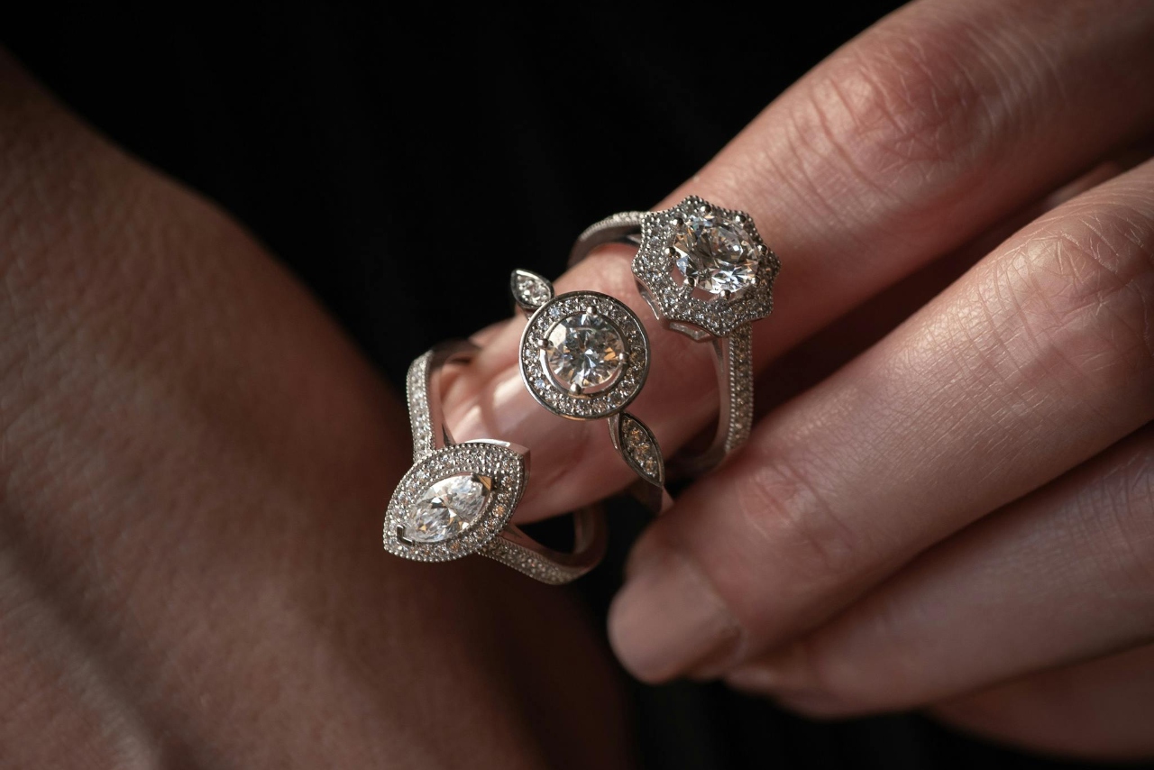 A hand with three engagement rings looped onto the pointer finger, each with a different shaped diamond.