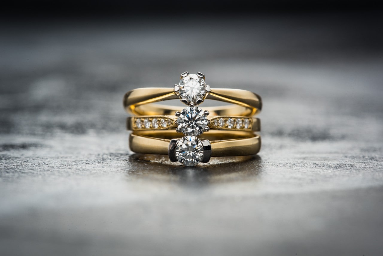 Three gold rings with sparkling diamonds stacked on a reflective surface.