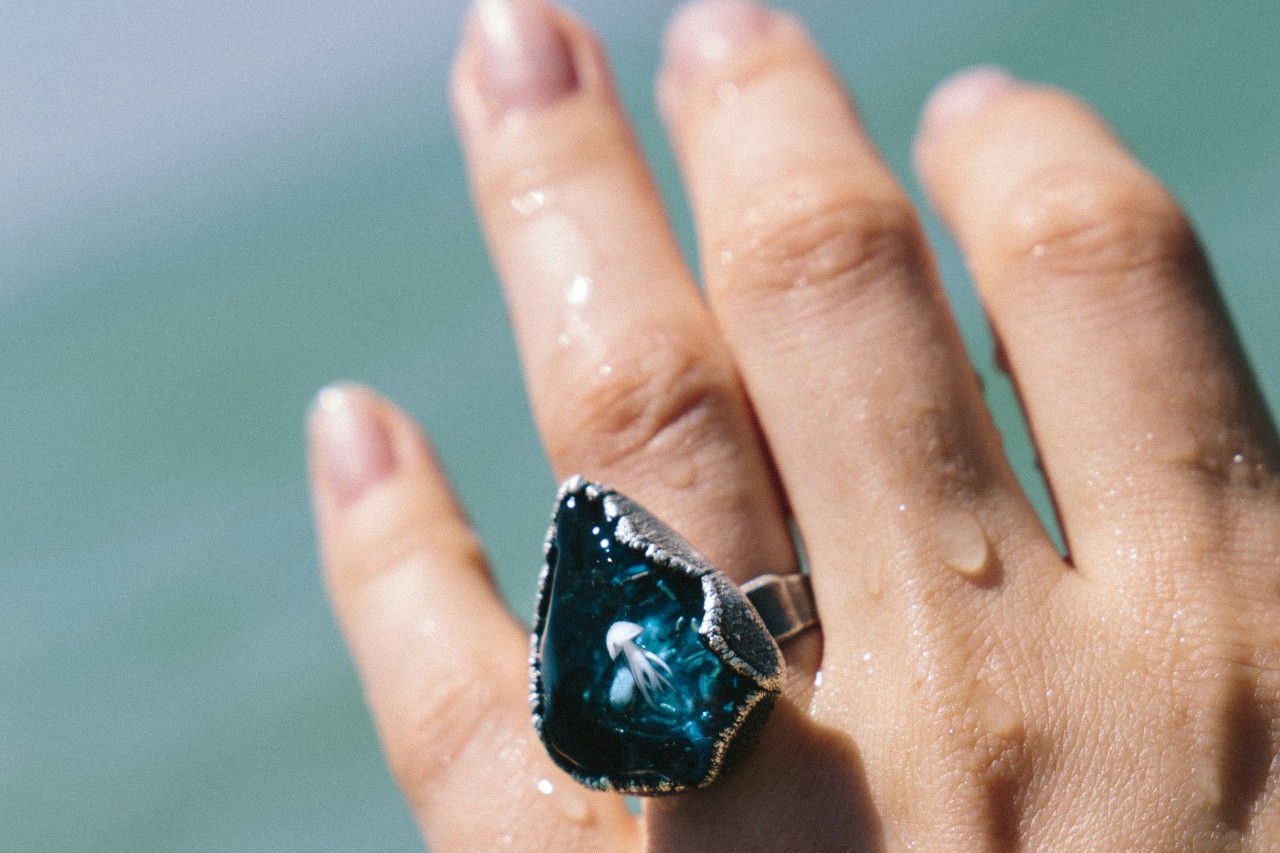 Close-up of a hand adorned with a large, blue gemstone ring, wet with water droplets.