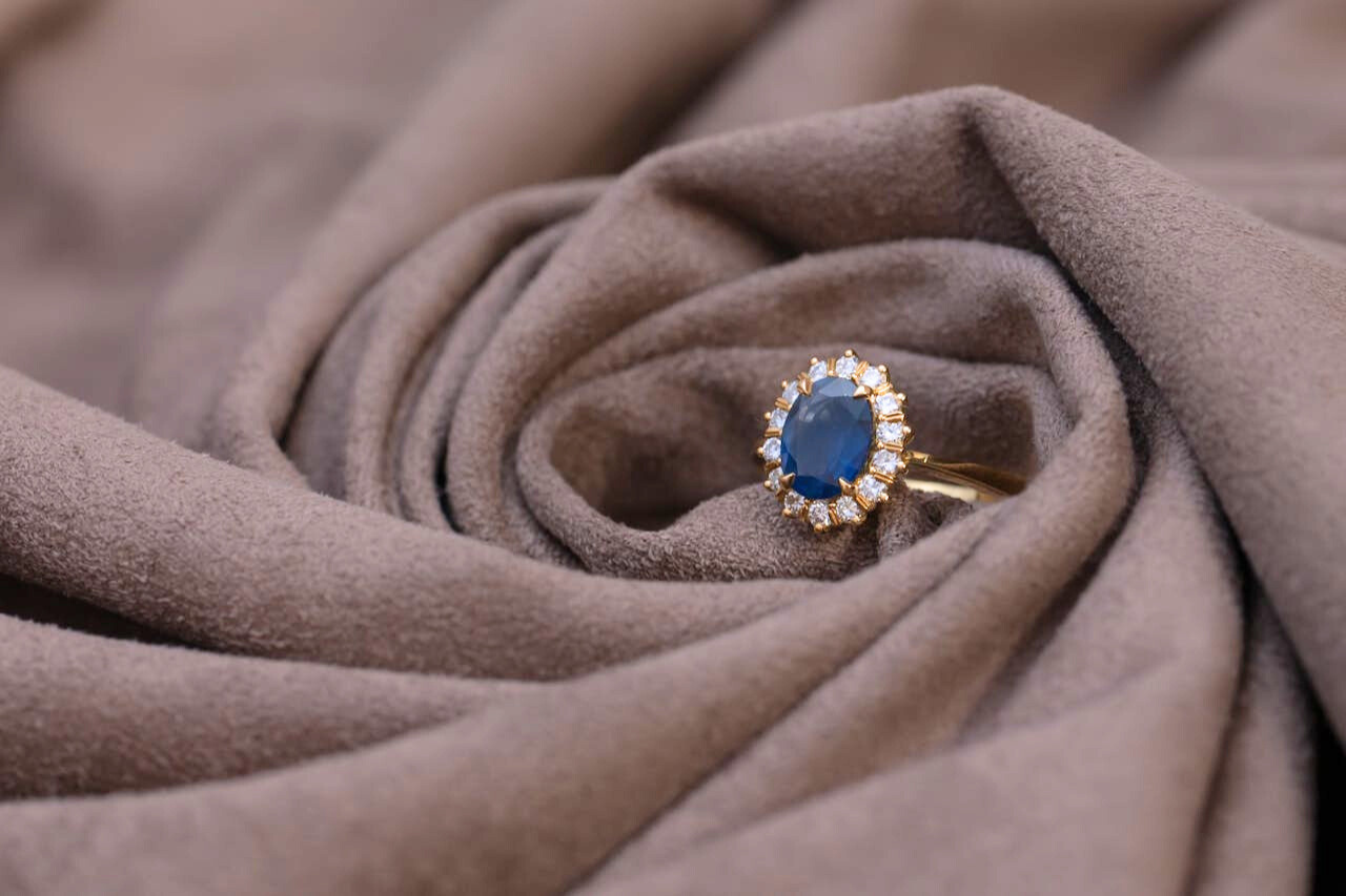 A sapphire engagement ring with a beautiful halo, wrapped inside of a piece of cloth.