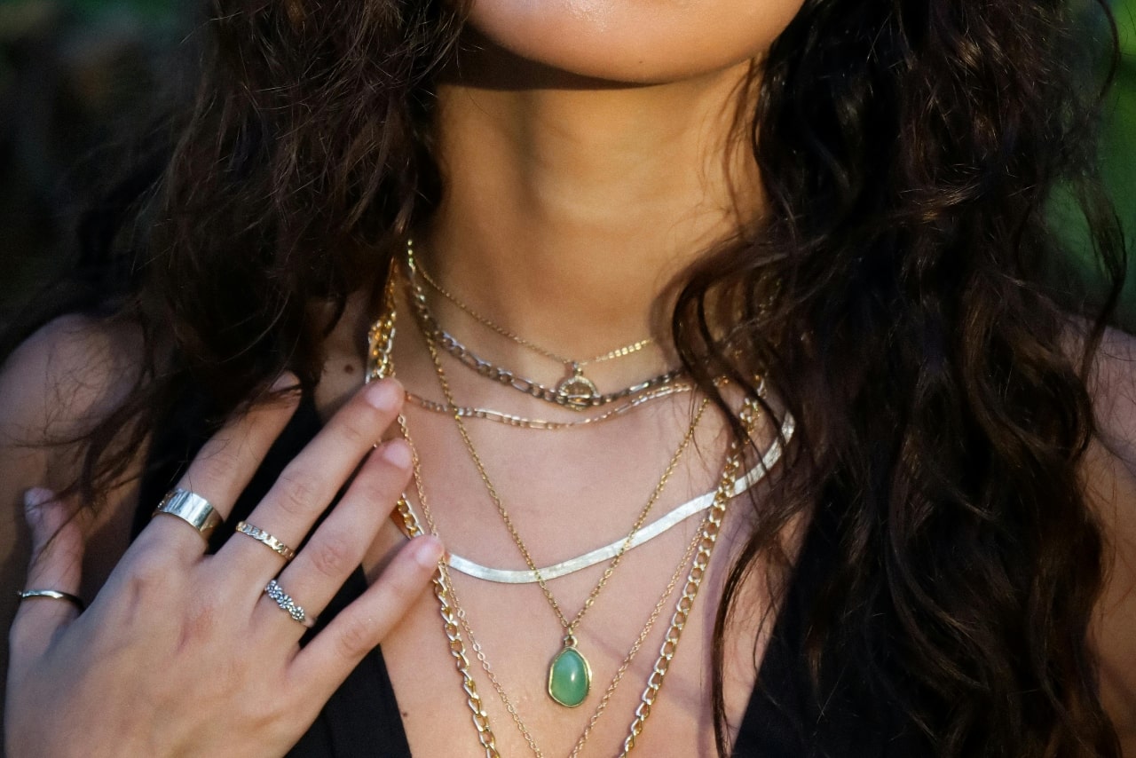 A close-up of a woman wearing seven layered necklaces of varying lengths and styles.