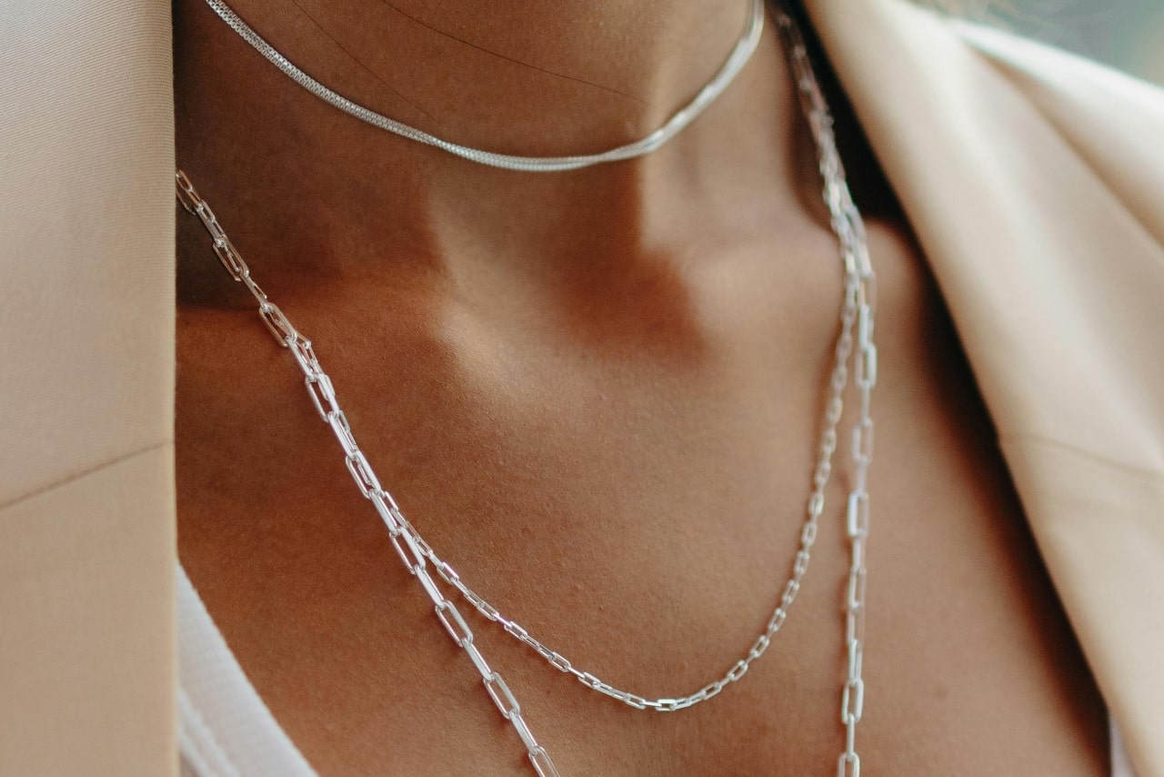 A close-up image of a woman’s neckline adorned with three silver layered necklaces