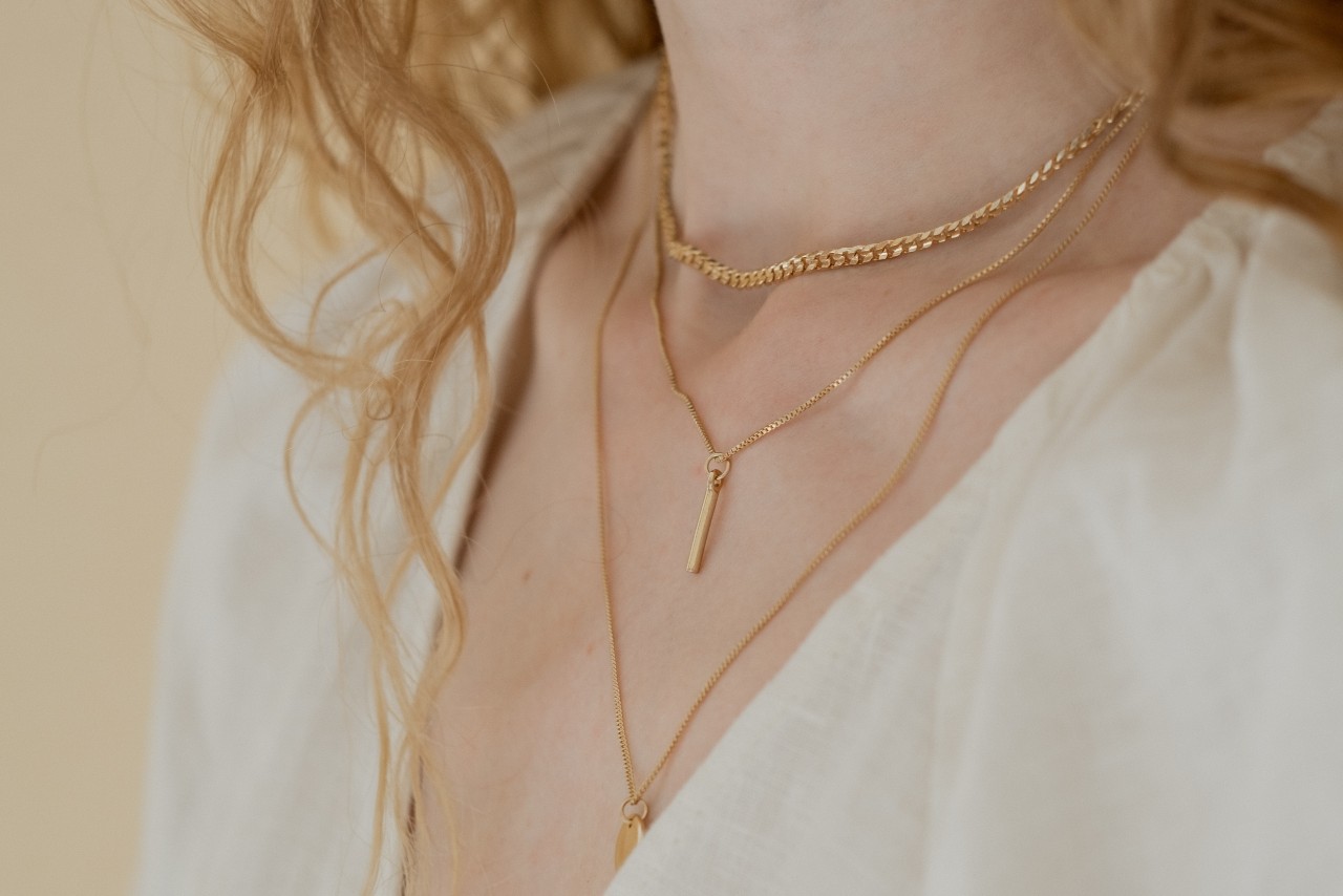 A close-up image of a woman’s neckline adorned with three layered gold necklaces