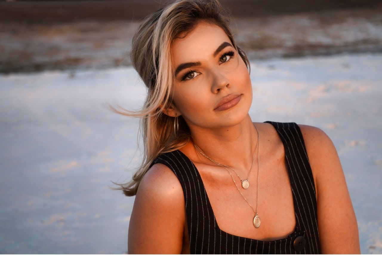 A woman on the beach wearing two gold layered pendant necklaces