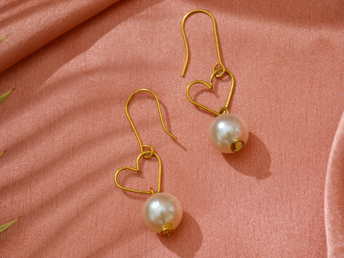A pair of gold dangle earrings with pearls, the wire above the pearls shapes into hearts.