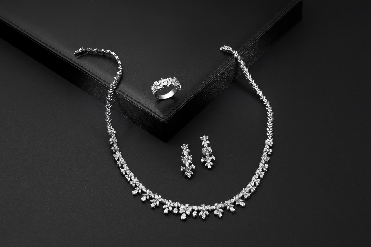 A white gold diamond jewelry set on a black background includes a sparkling necklace, a ring, and matching earrings
