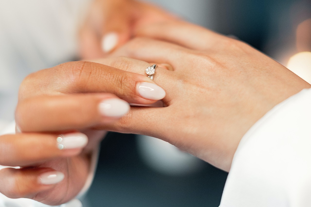 Close-up of a manicured hand placing a ring on another hand.