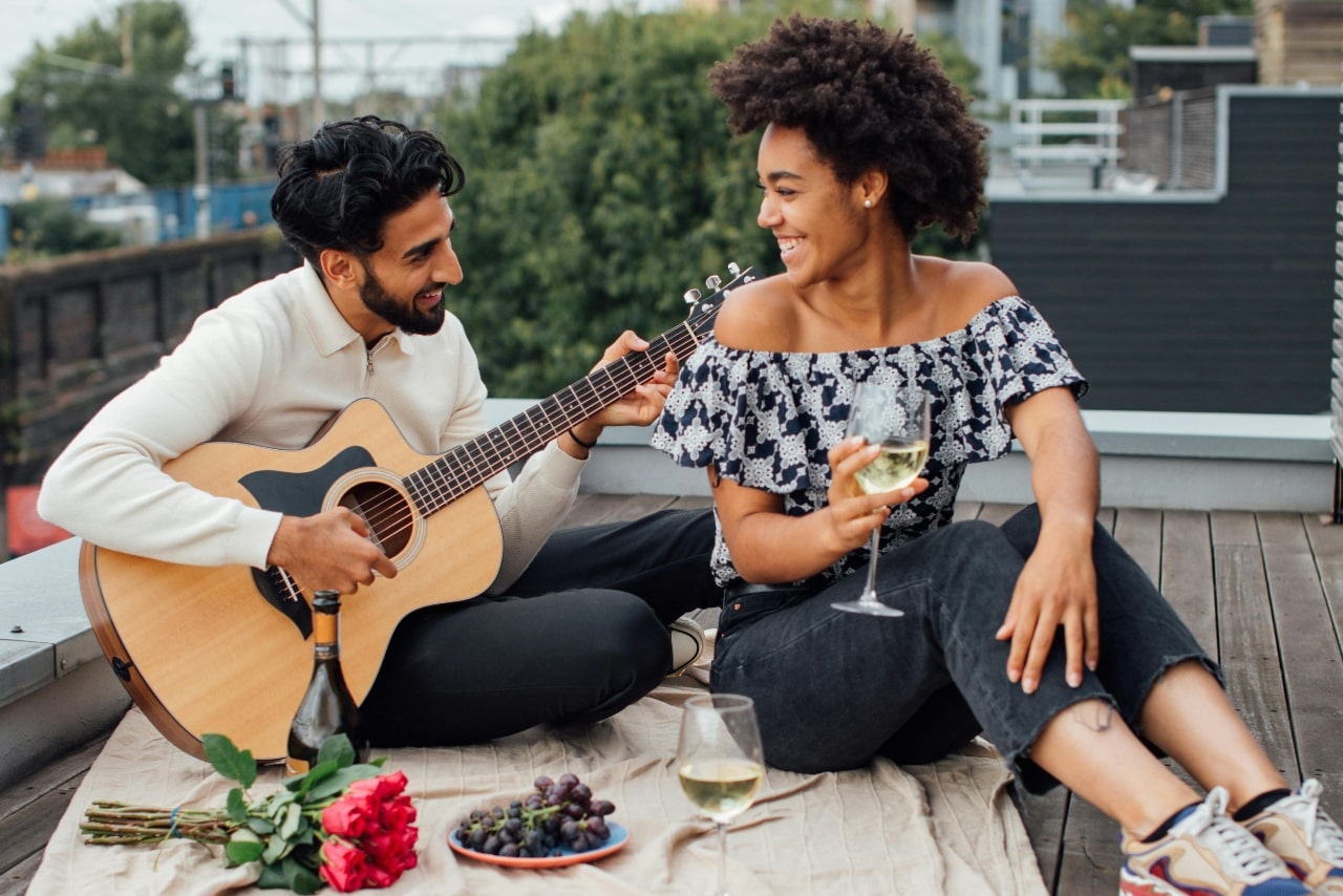 A couple sharing a rooftop date night with guitar, wine, roses, and grapes