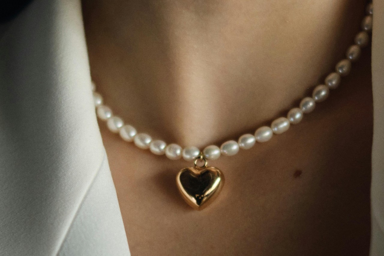 A close-up image of a woman’s neckline adorned with a pearl heart necklace.