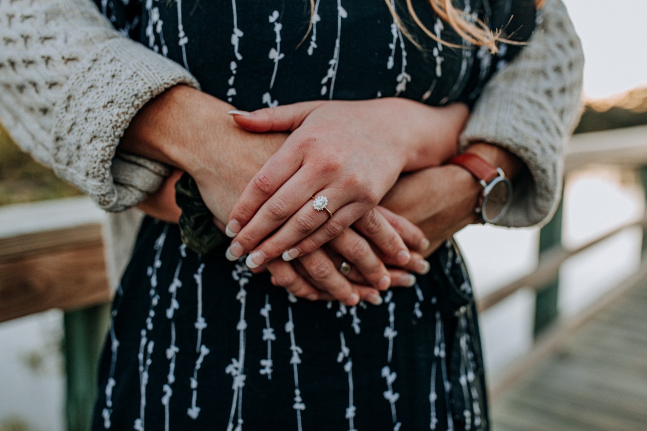 A close-up of a couple embracing on the bridge, showcasing woman’s french manicure and oval cut rose gold solitaire diamond engagement ring.