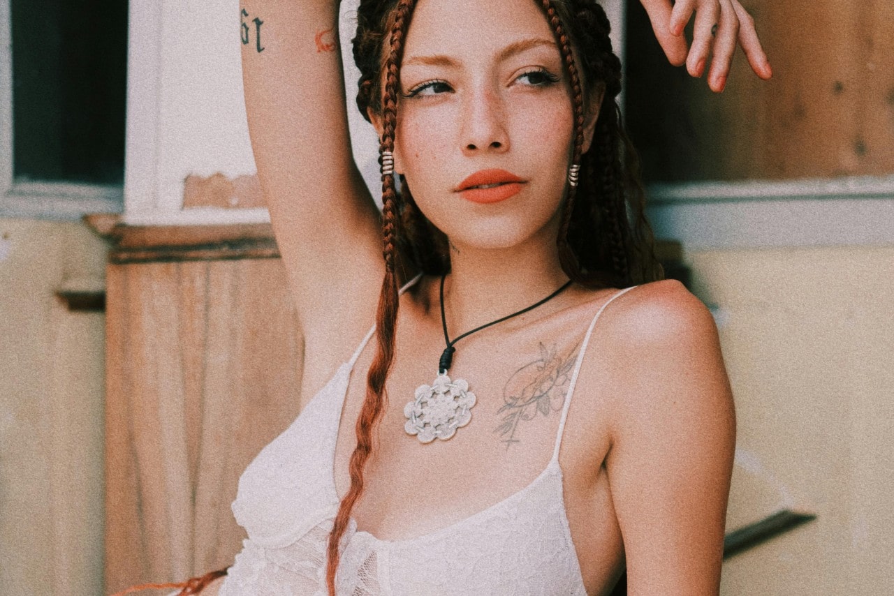 A woman in a white tank top and a large flower pendant necklace