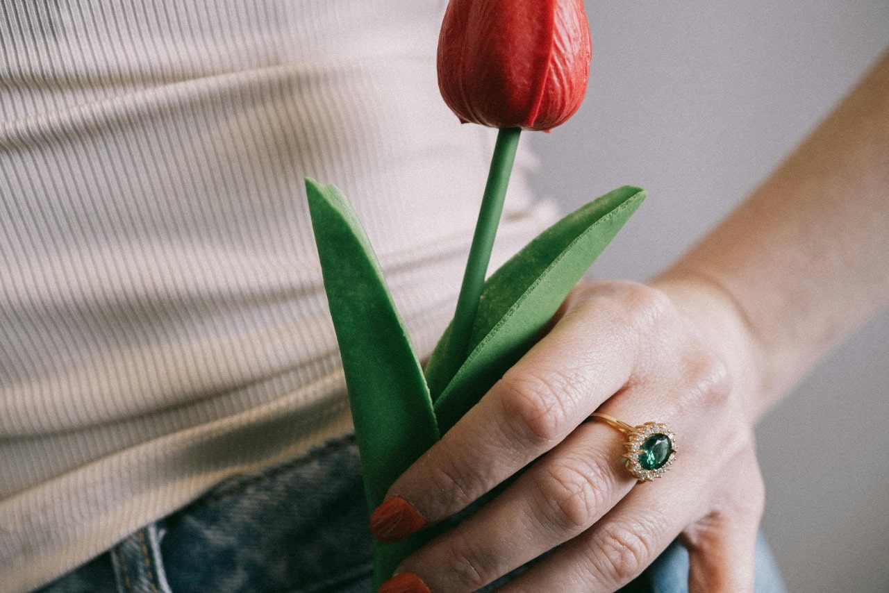 A close-up of a woman wearing an emerald ring putting a tulip in her pocket.