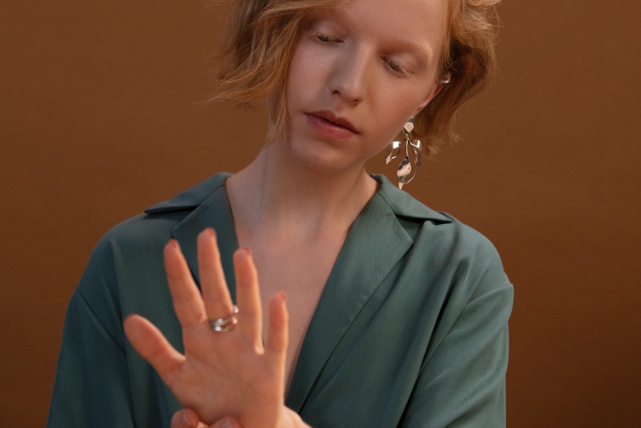 A woman with ginger hair with floral earring admiring her rings, sitting against a dark orange wall