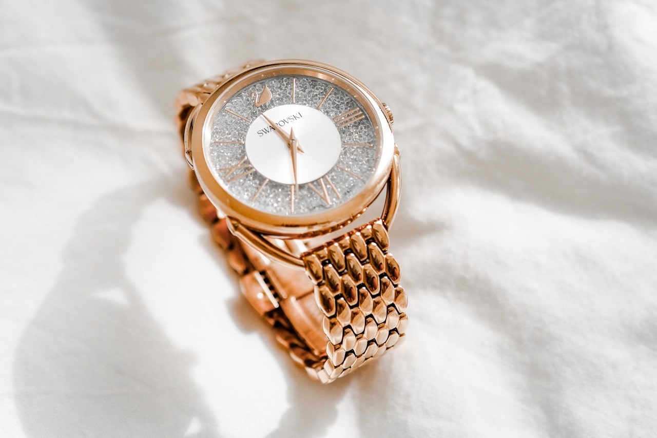 Rose gold wristwatch with a glittery, textured face and Roman numerals on a soft white fabric background.