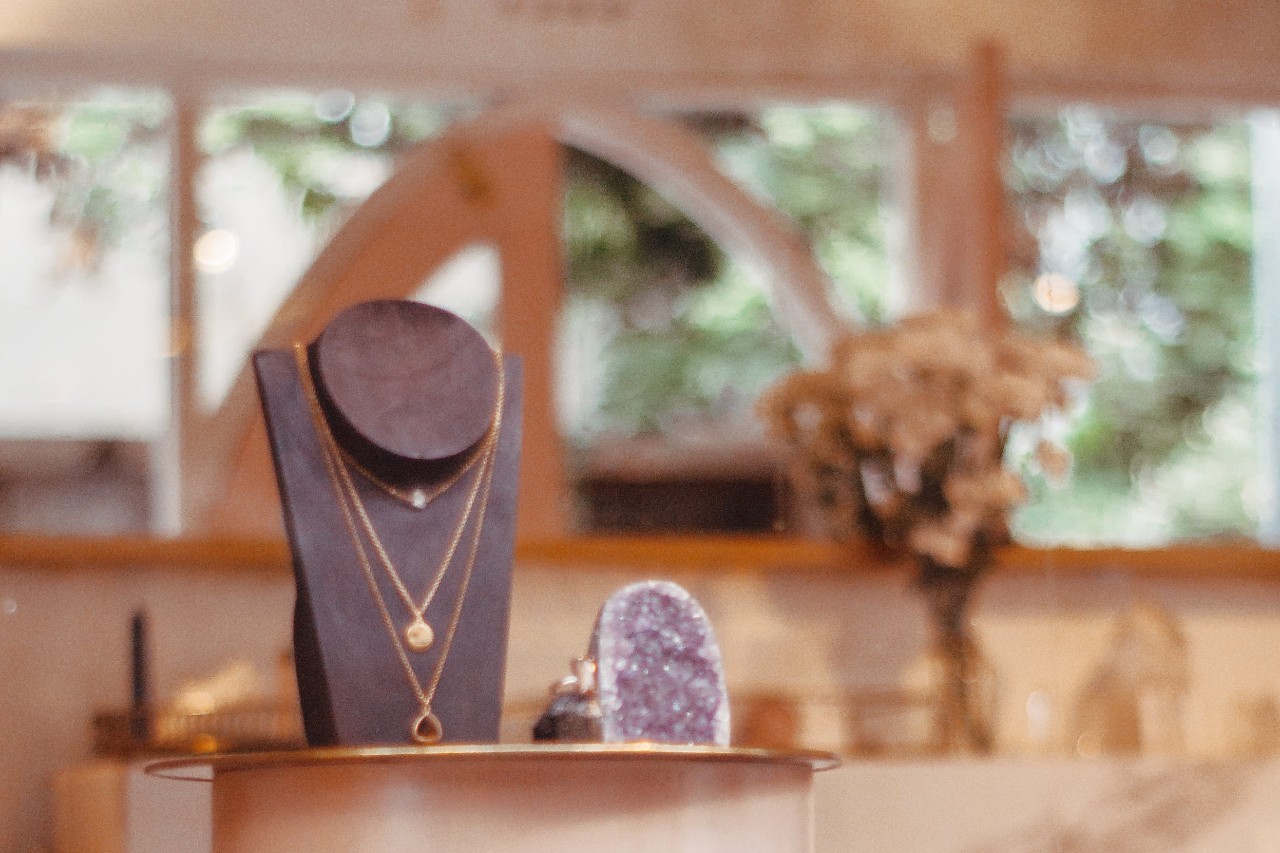 Elegant jewelry display with layered gold necklaces on a stand, set in a softly lit luxurious boutique.