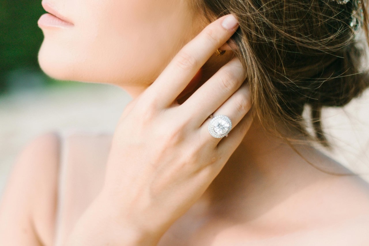 a woman with her hand in her hair wearing a large diamond halo white gold engagement ring