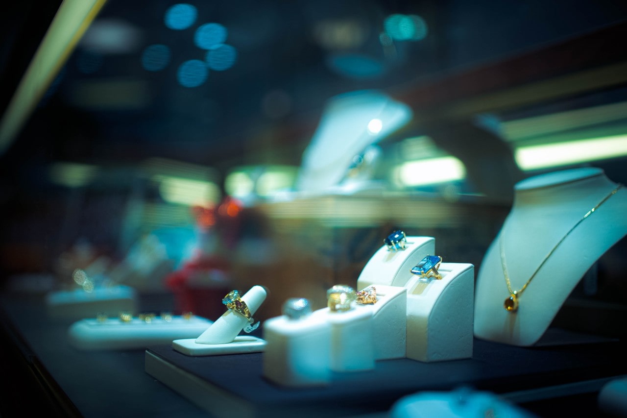 A view of a jewelry store display under night lighting featuring colorful gemstone necklaces and rings.