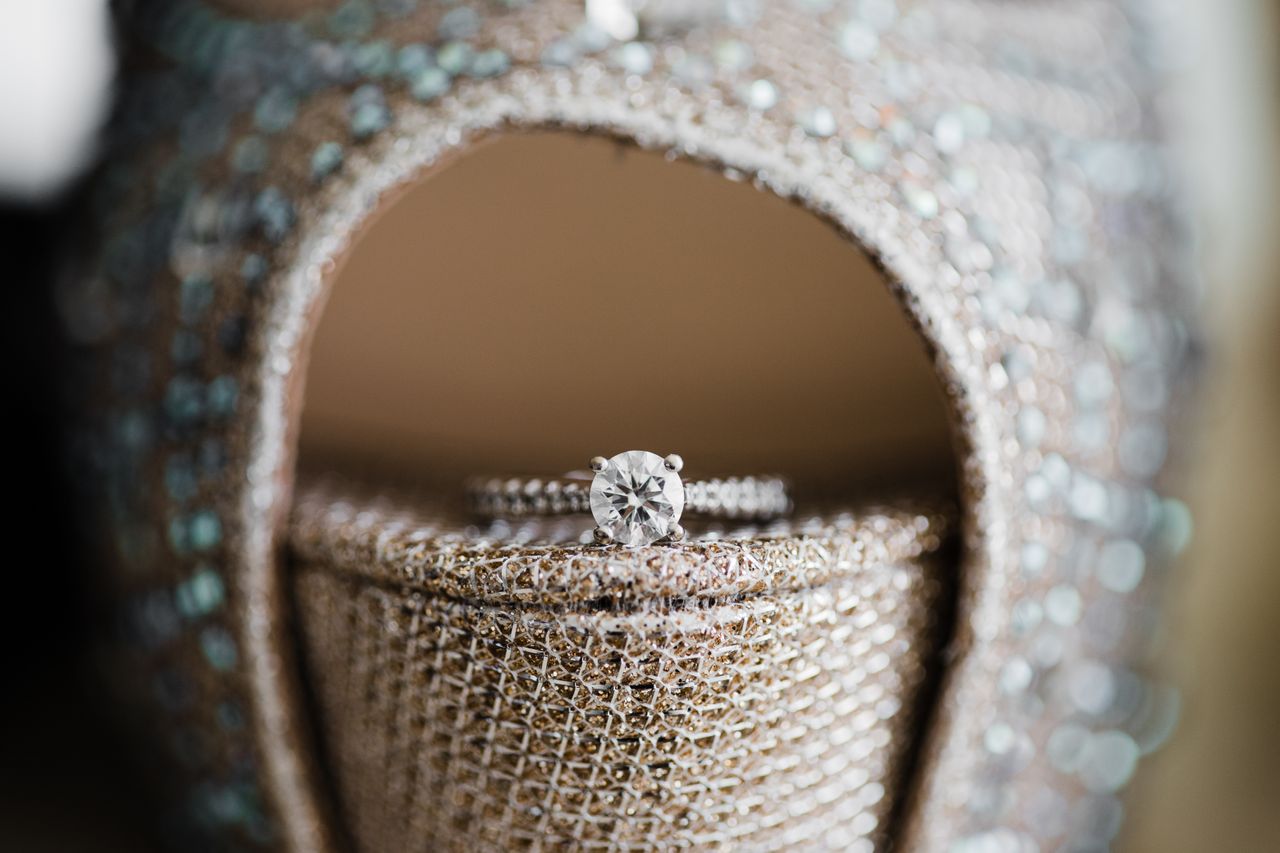 A close-up of a sparkling diamond ring delicately placed on the heel of a shimmering, sequined shoe.
