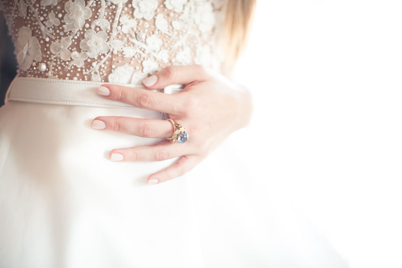 Close-up of a bride's waist with lace floral dress and a hand resting on it, wearing a jeweled ring.