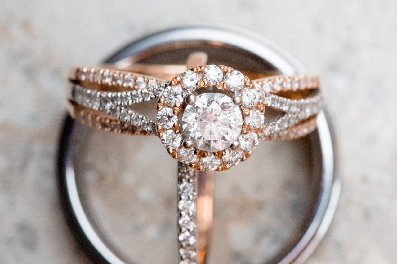 Close-up of a rose gold engagement ring with a central diamond, encircled by smaller diamonds, resting on a silver wedding band.