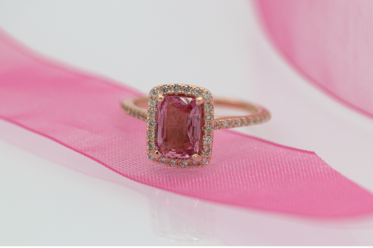 A halo pink gold ring with square pink stone on a pink piece of clothing against a white background