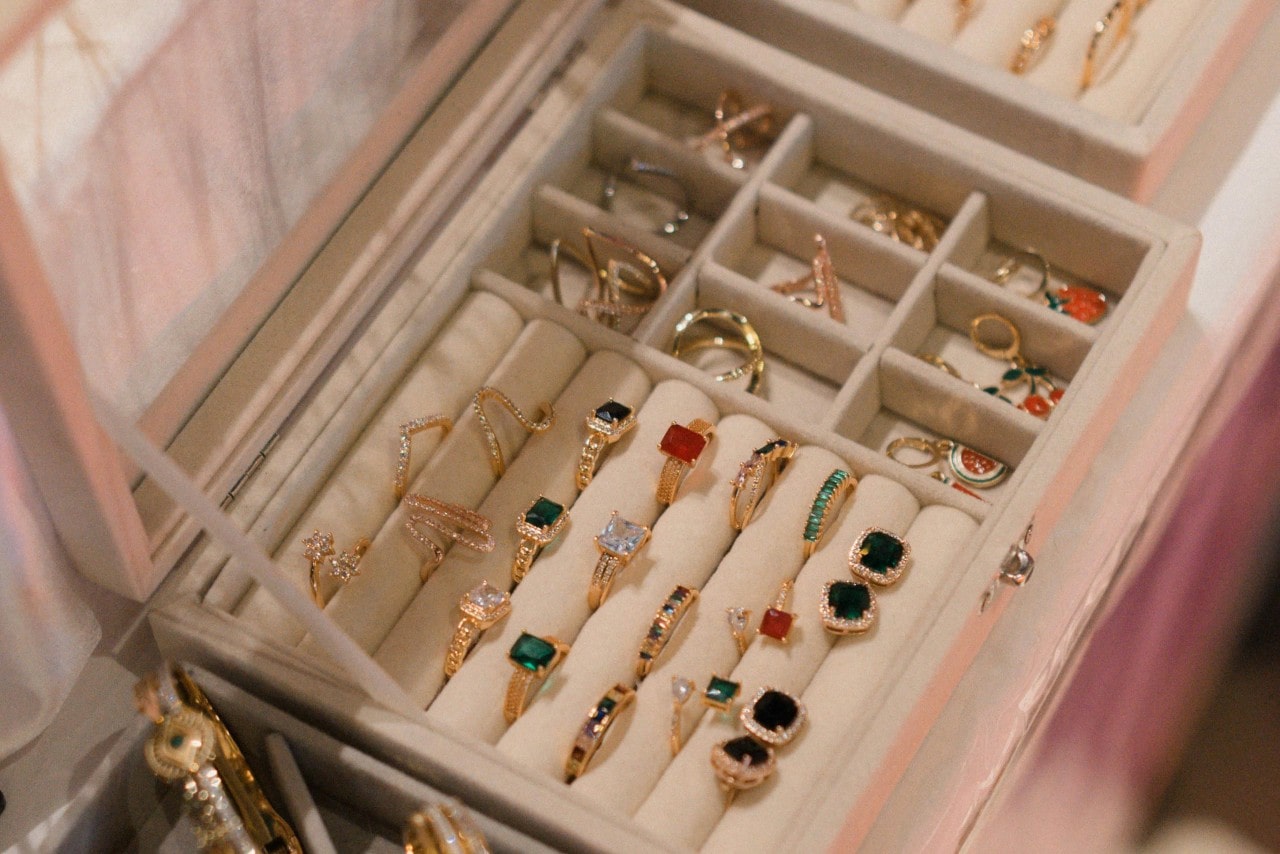 An organized jewelry box displays an assortment of gold rings with colorful gemstones and intricate designs.