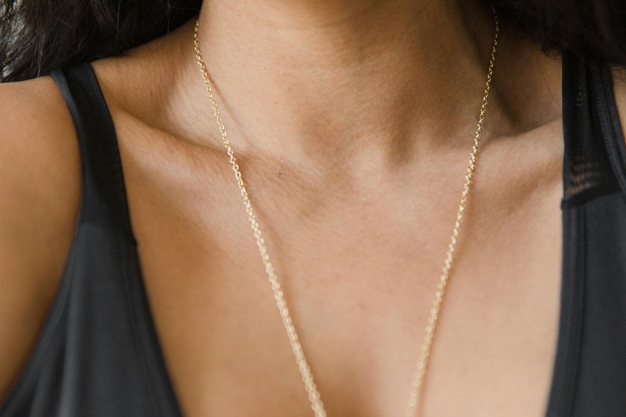 A close-up of a woman’s decolletage, with emphasis on the delicate gold chain draped over it.
