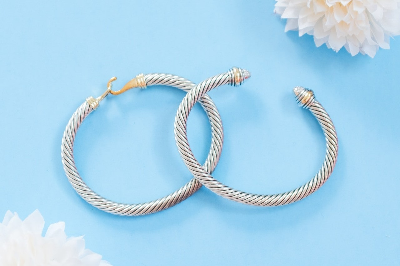 Two silver rope style bangles laying on a bright light blue surface with white flowers in the corners.