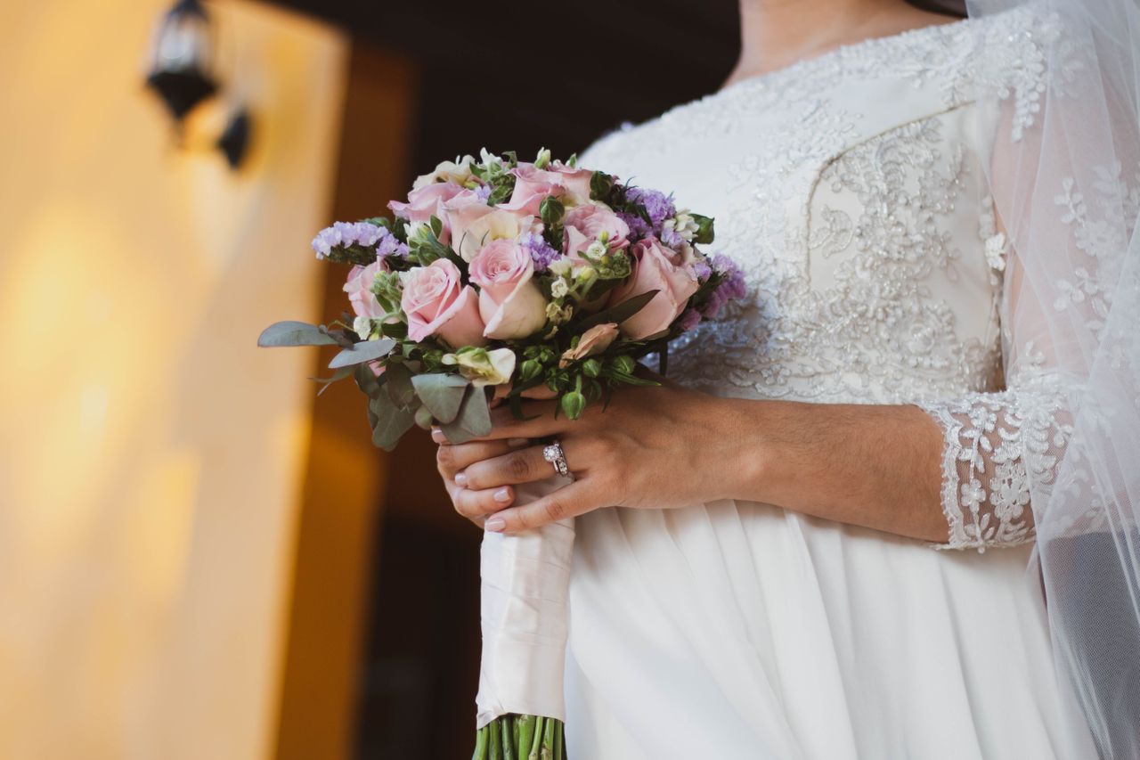 A bride in a lace dress holding a bouquet of flowers, showcasing dazzling white gold bridal set – engagement ring and wedding band. A bride in a lace dress holding a bouquet of flowers, showcasing dazzling white gold bridal set – engagement ring and wedding band.