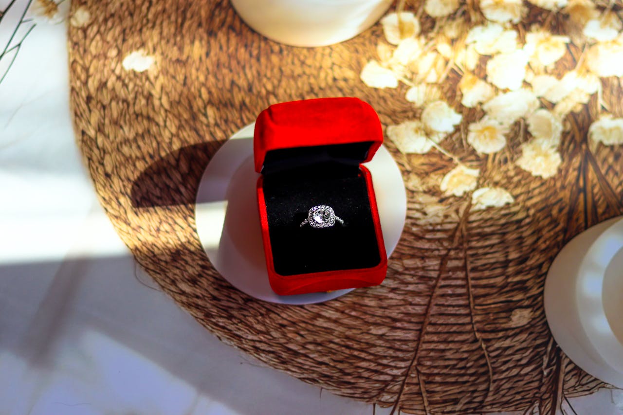 A white gold halo diamond engagement ring inside the black and red velvet box on top of the tupperware
