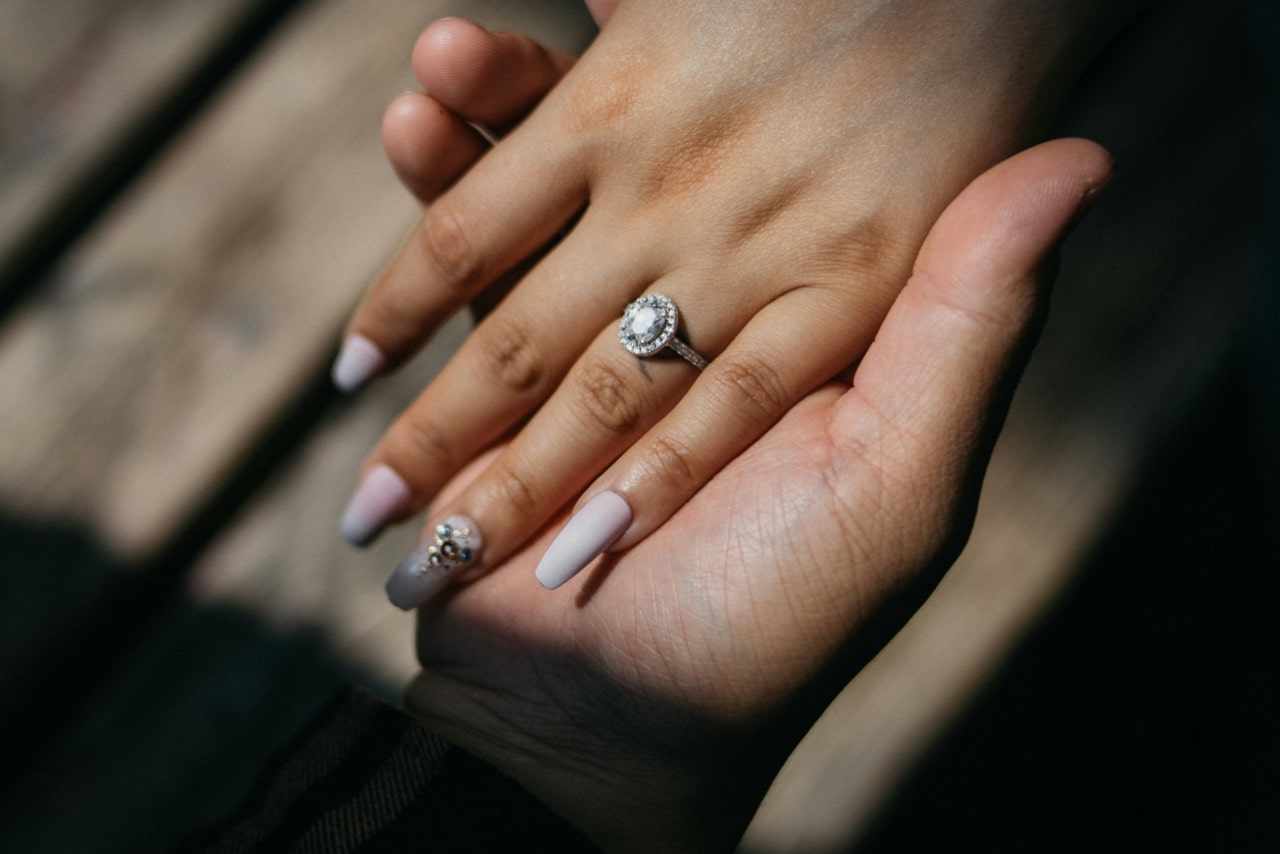 A close up of hand with manicure nails, showcasing white gold halo engagement ring