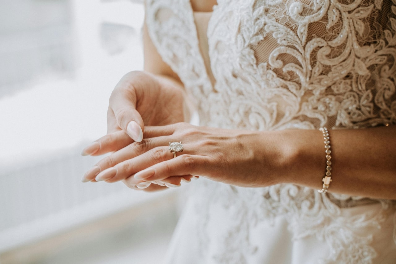 Close-up of a bride in an intricate white lace gown, gracefully adjusting her ring.