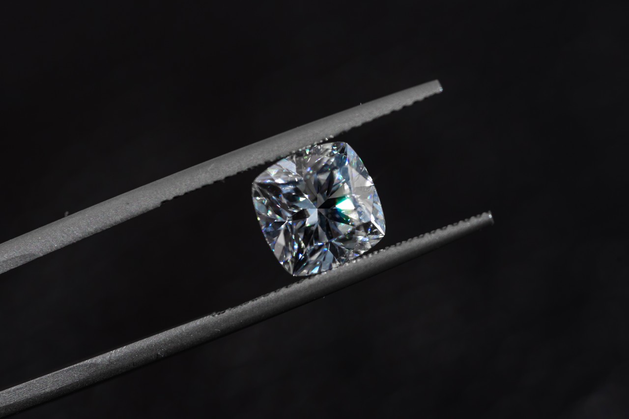 A cushion diamond being held between jeweler tweezers A cushion diamond being held between jeweler tweezers