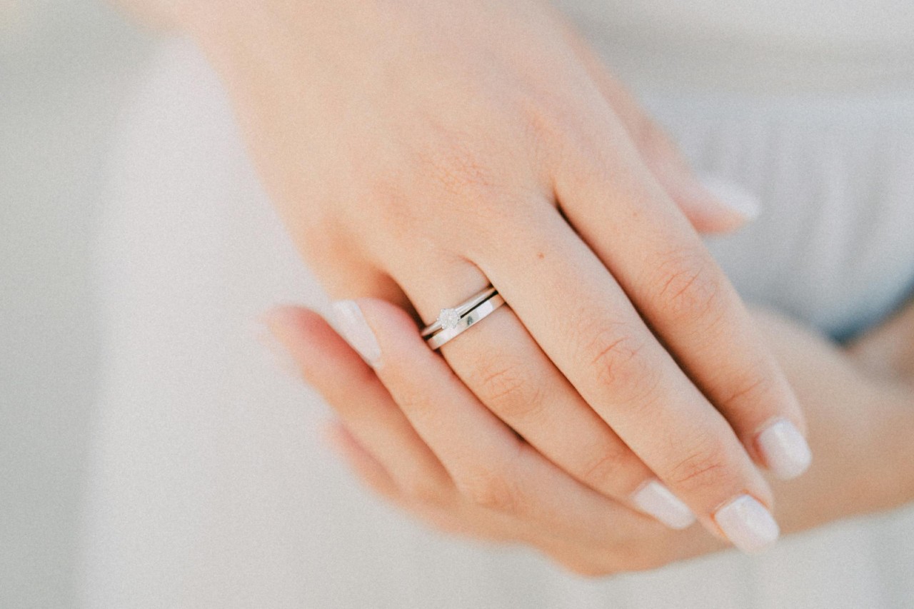 A woman’s hands, one of which is adorned with a white gold diamond ring and wedding band. A woman’s hands, one of which is adorned with a white gold diamond ring and wedding band.