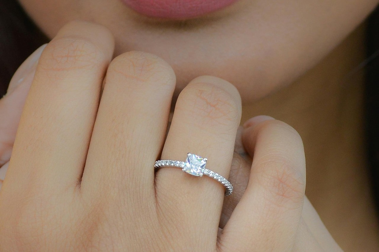 A woman wearing a platinum engagement ring, her hand raised to her chin. A woman wearing a platinum engagement ring, her hand raised to her chin.