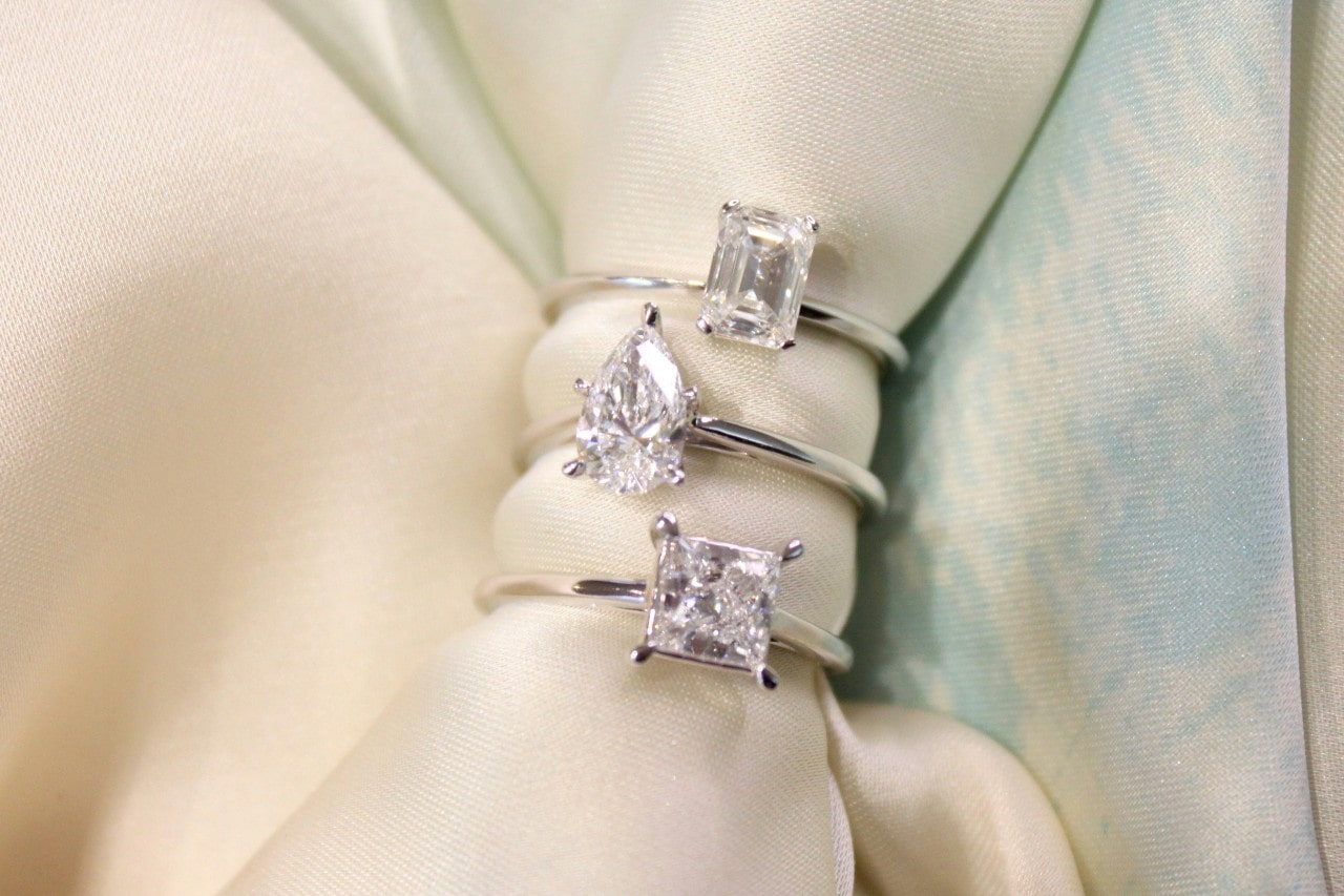 three diamond engagement rings with a cloth threaded through three diamond engagement rings with a cloth threaded through