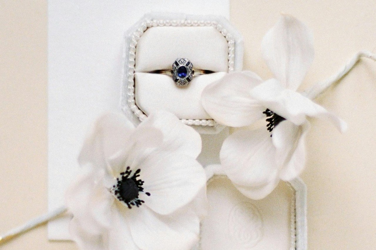 a trendy engagement ring in a white box next to white flowers a trendy engagement ring in a white box next to white flowers