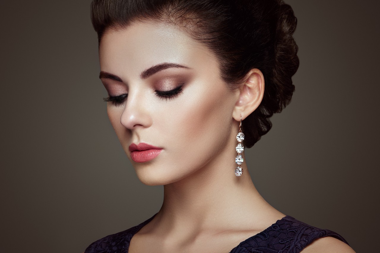A woman with a swept up hair do and pretty make-up is wearing long dangling diamond earrings