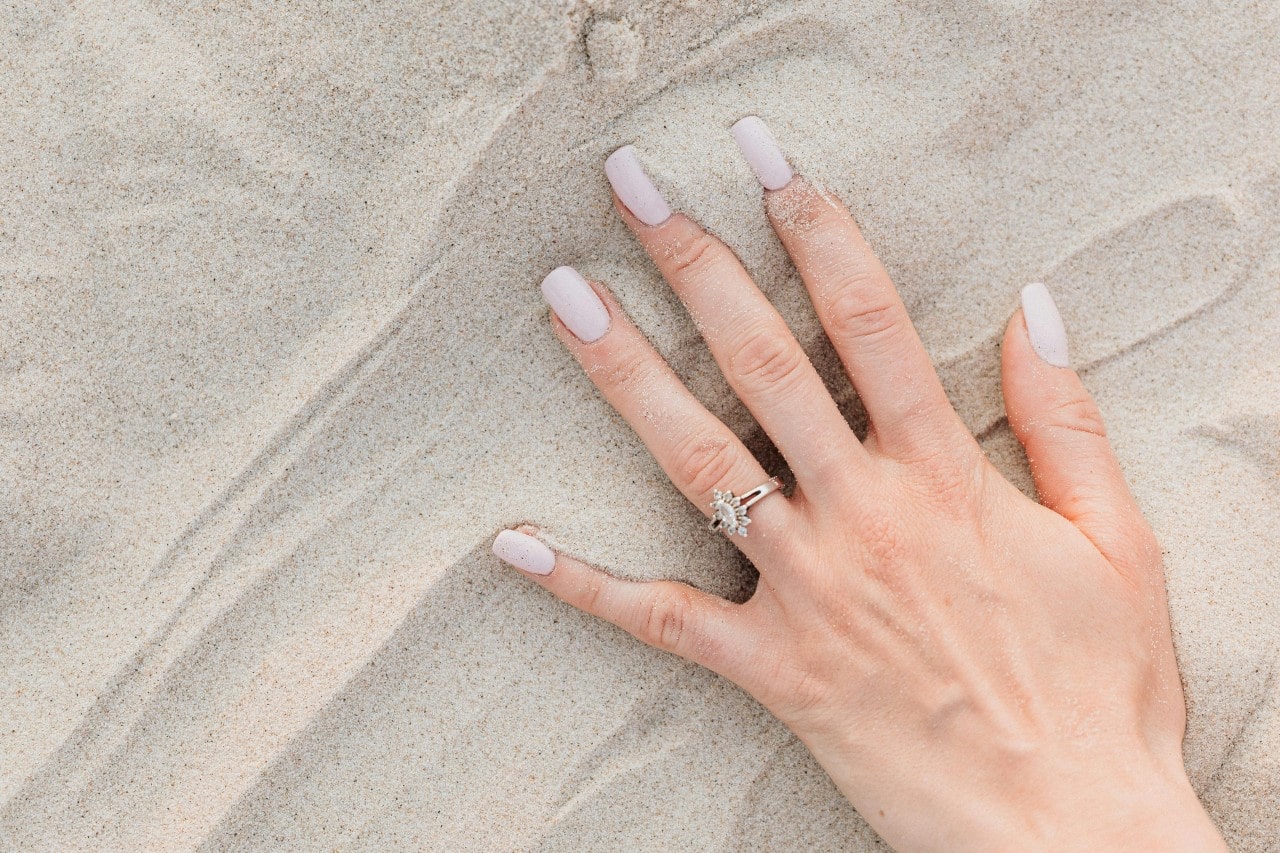 A woman swipes her hand through the sand, wearing her engagement ring.