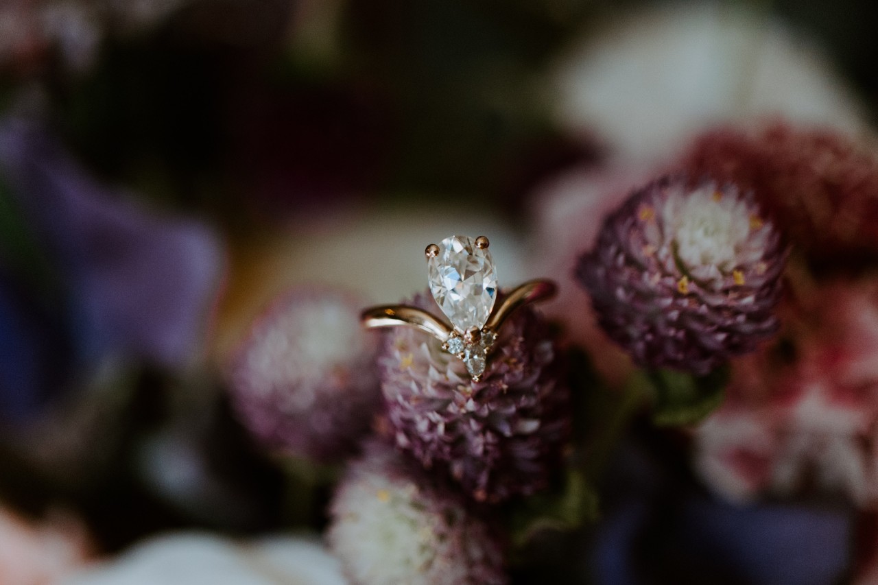 A yellow gold engagement ring perched on a flower, featuring a pear shaped center stone