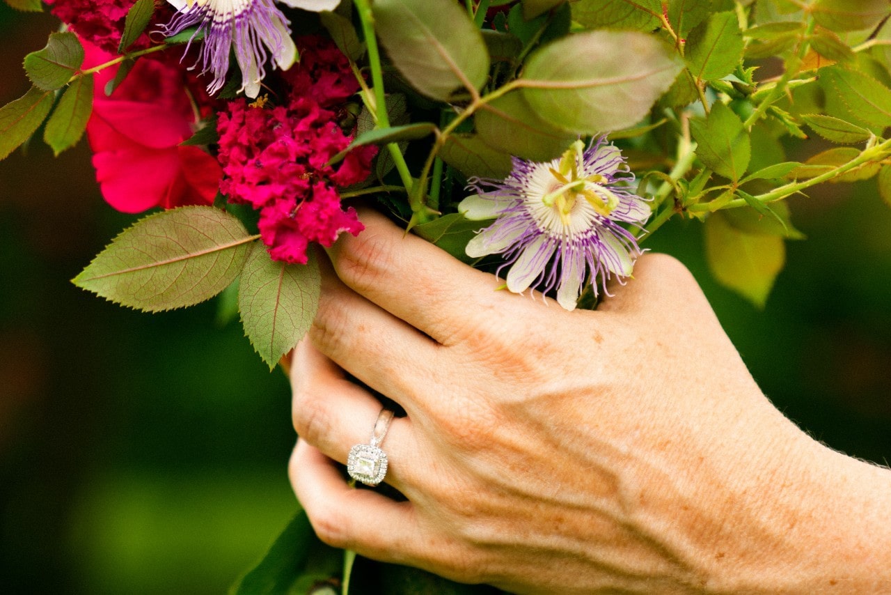 a hand holding a floral bouquet and wearing a white gold halo engagement ring