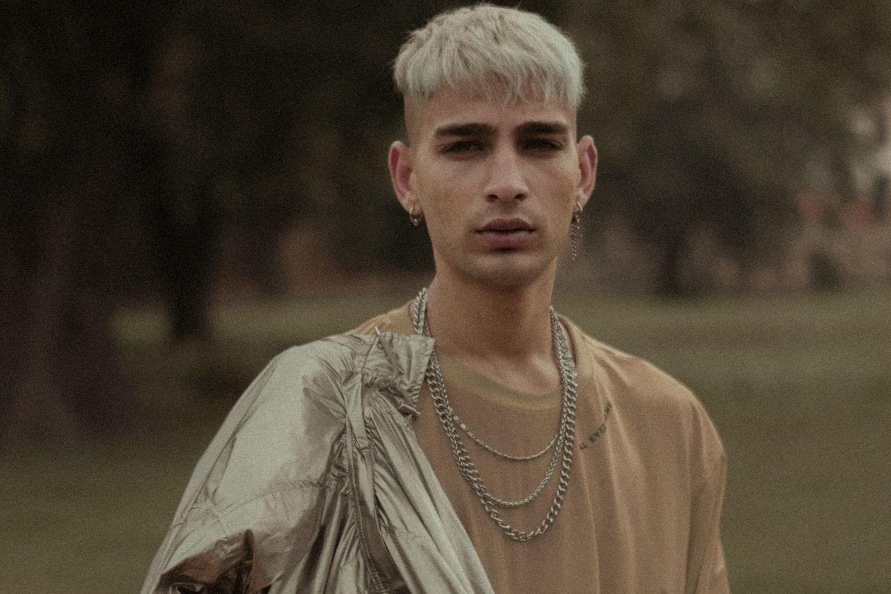 A young man wearing three white gold chain necklaces while outside.