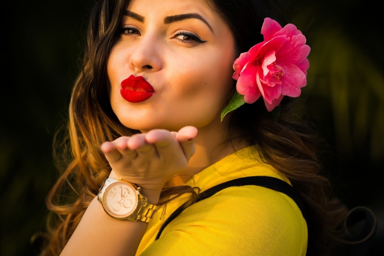lady wearing a watch and a flower in her hair, blowing a kiss at the camera