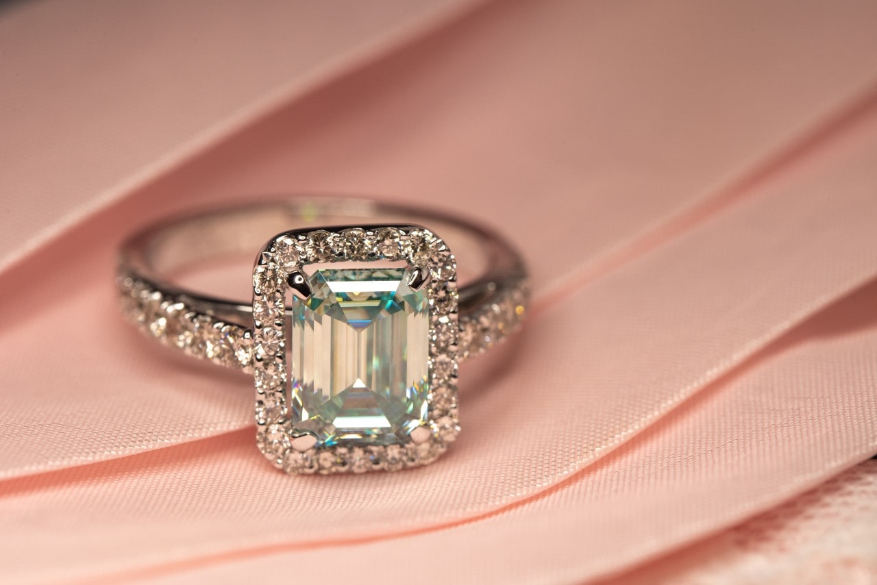 a white gold engagement ring featuring an emerald cut diamond and a halo of accent stones