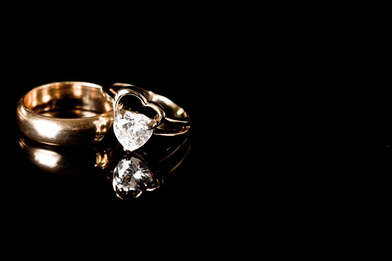 A gold heart-shaped engagement ring and wedding band sit on a black background.