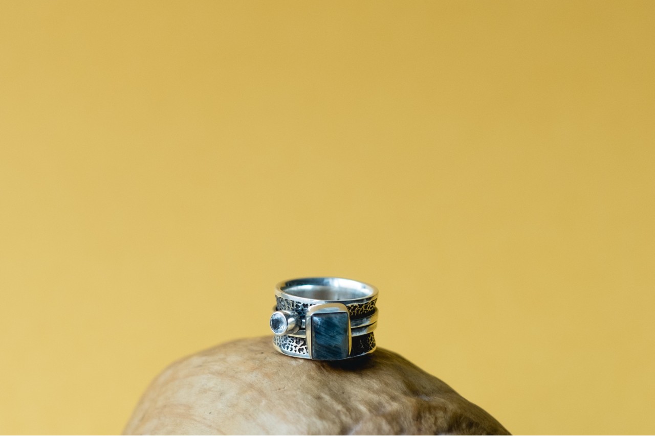 A silver fashion ring with intricate details and a blue gemstone