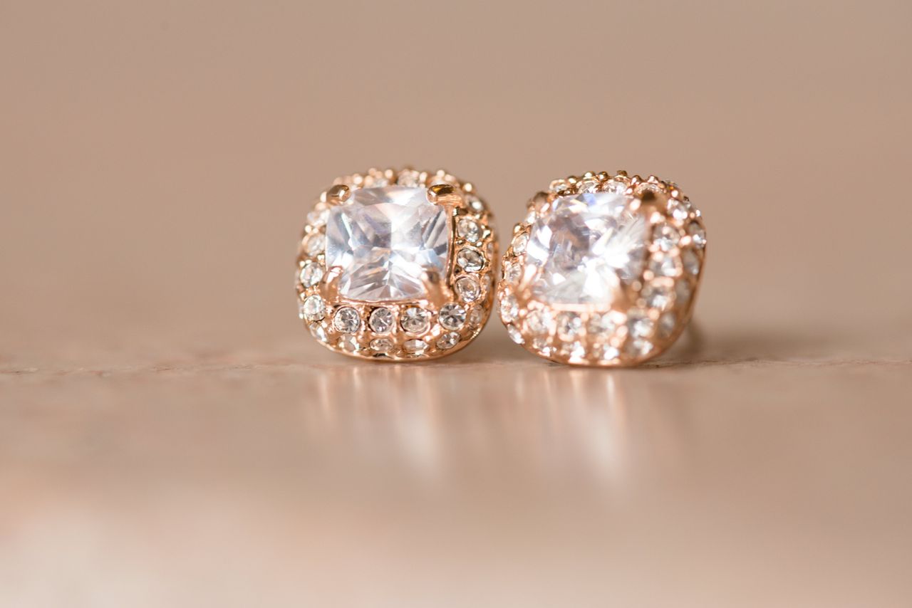 A pair of rose gold, diamond halo earrings on a beige surface